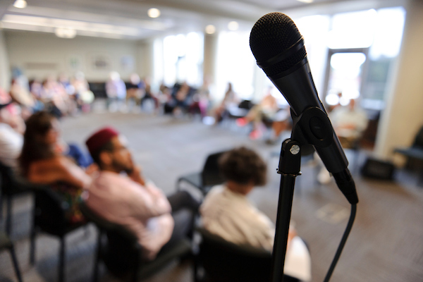 A microphone fills the foreground in front of a diverse group of more than 25 educators and community leaders.