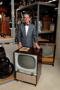James Baughman, SJMC professor emeritus and department chair, posing with a 1953 Sylvania, foreground, and 1958 RCA television sets in the Wisconsin Historical Society's warehouse.