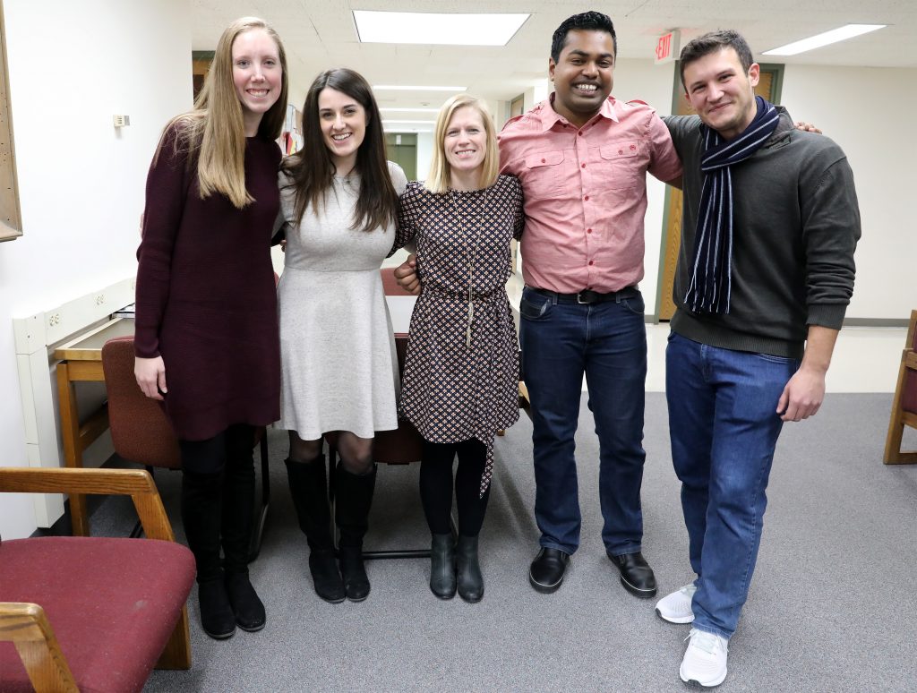 Teaching faculty Stacy Forster with two male and two female students graduating from the Professional MA program