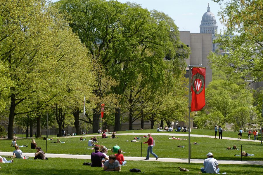 "W" crest banners hang on Bascom Hill as pedestrians cross walkways and people relax on the hill during spring.