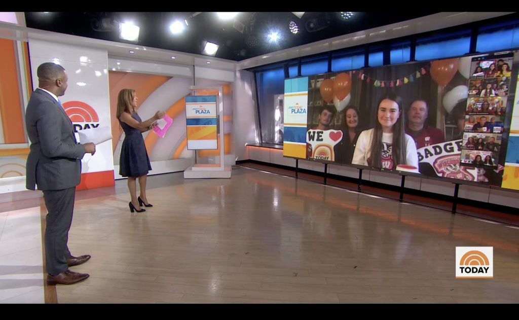 Two anchors in a studio stand in front of a video monitor displaying Gracie Lund and her family