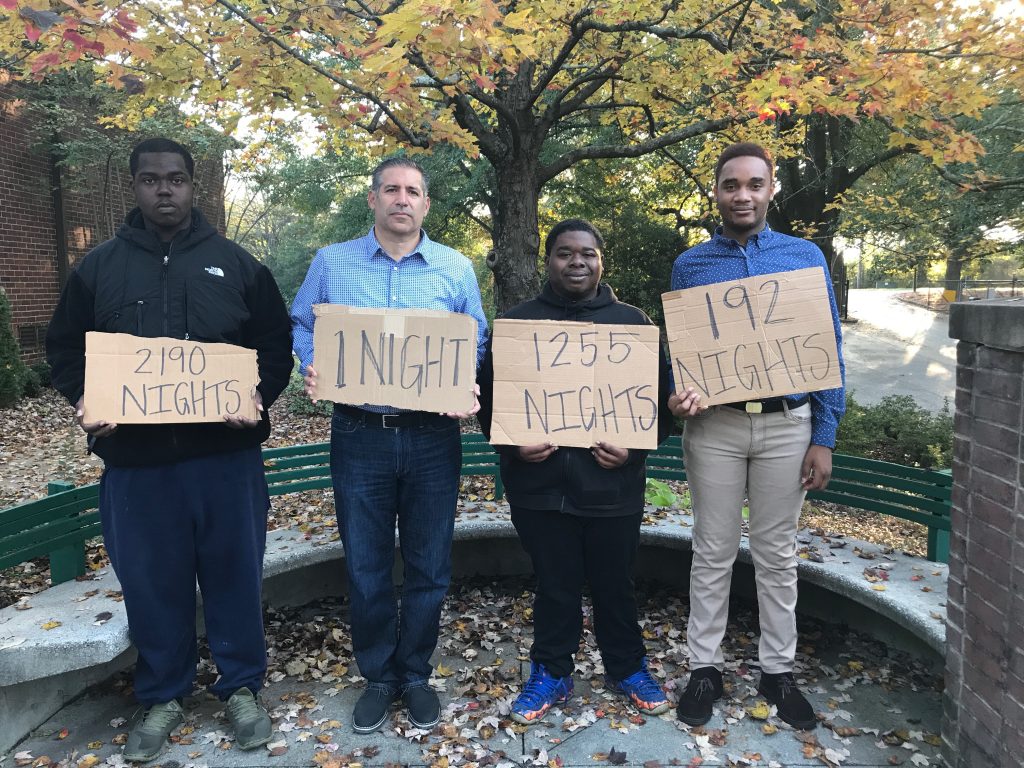 Ben Deutsch holding a sign reading 'one night', with three young men holding signs reading '2190 nights', '1255 nights' and '192 nights'.