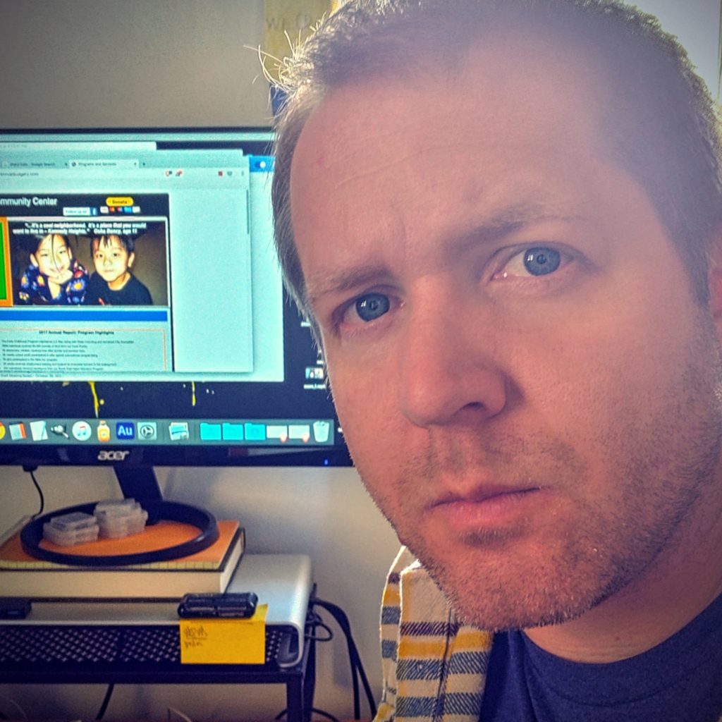 A man facing the camera in front of a computer monitor with video editing software displayed.