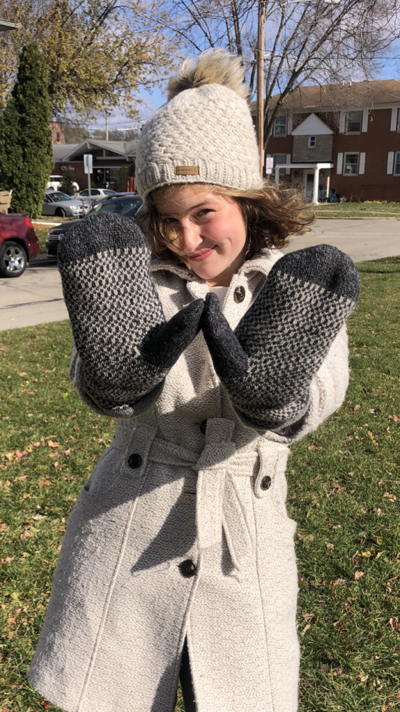 A woman in a winter coat, hat and mittens holds up her hands in the shape of the letter W