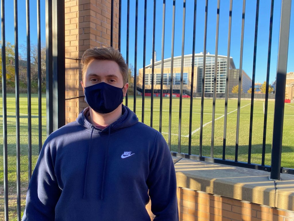 A man in a face mask stands in front of the gate outside the empty UW athletic practice fields