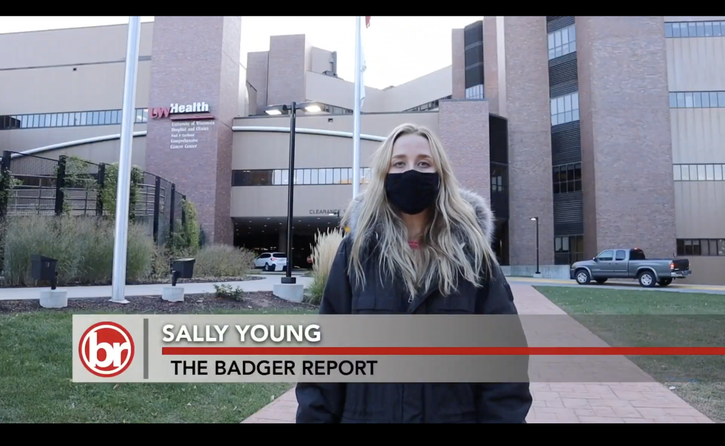 A woman in a face mask stands in front of the UW Carbone Cancer Center