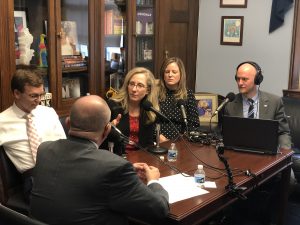 People sitting around a table in an office recording a podcast.