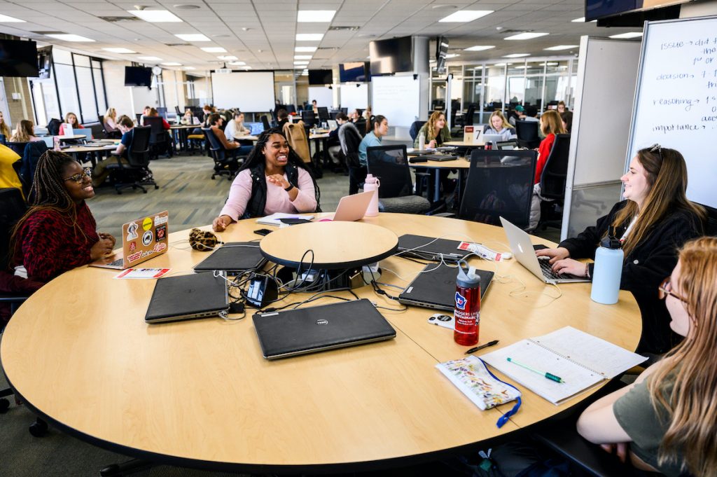 Student sitting around a table smiling and talking to one another.