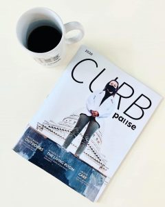 A print copy of Curb magazine laying on a white surface next to a cup of coffee.