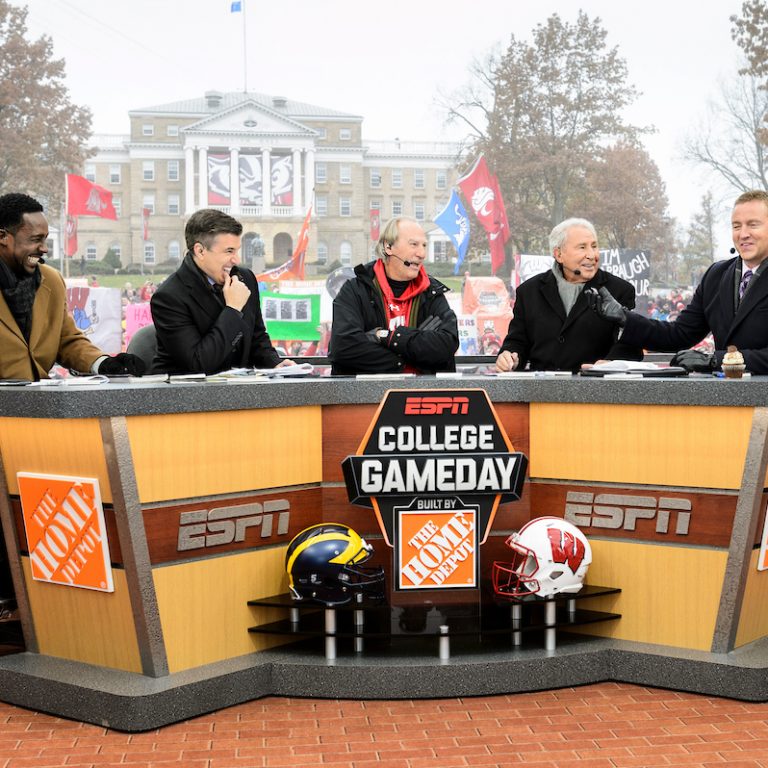 The anchors of ESPN College Game Day sit behind a desk with Bascom Hall in the background.