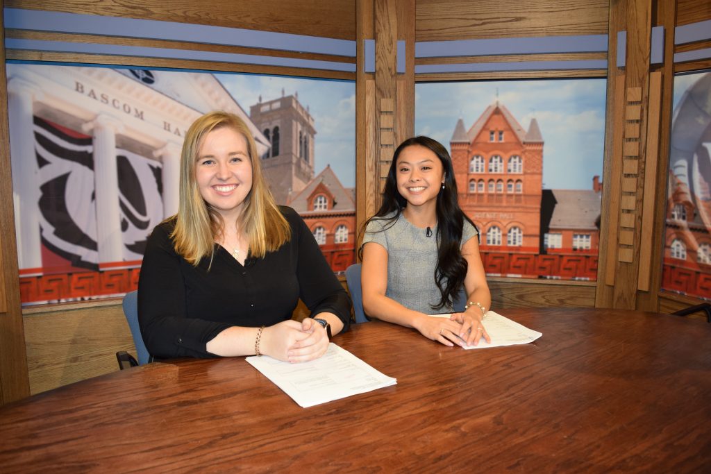 Two students sitting behind a news desk in the Wisconsin Public Television studios.