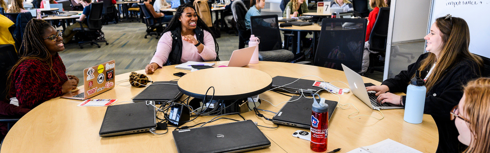 Four students sitting around a table with laptops smiling at one another.