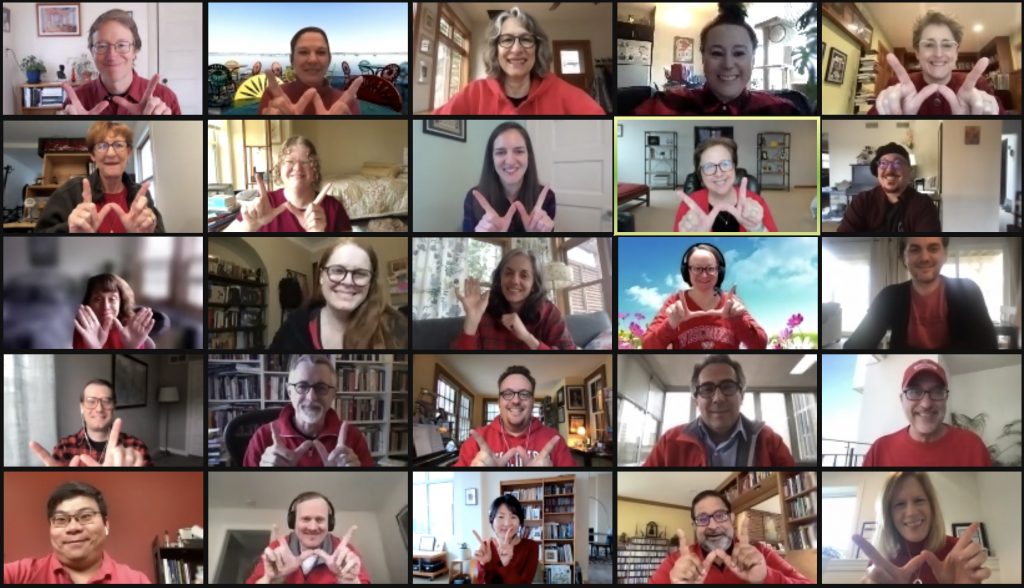 A screenshot of a Zoom meeting featuring the faculty and staff of the SJMC wearing red and holding their hands up in the shape of a 'W'.