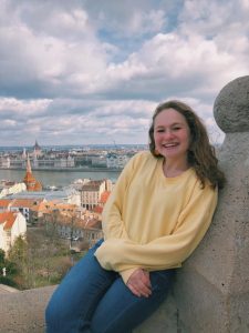 Elise Goldstein sits on a stone wall overlooking a landscape on a cloudy day.