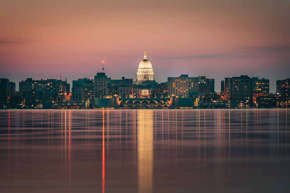 A panoramic shot of the Madison skyline from Lake Monona at dusk, featuring the Monona Terrace and Capitol building