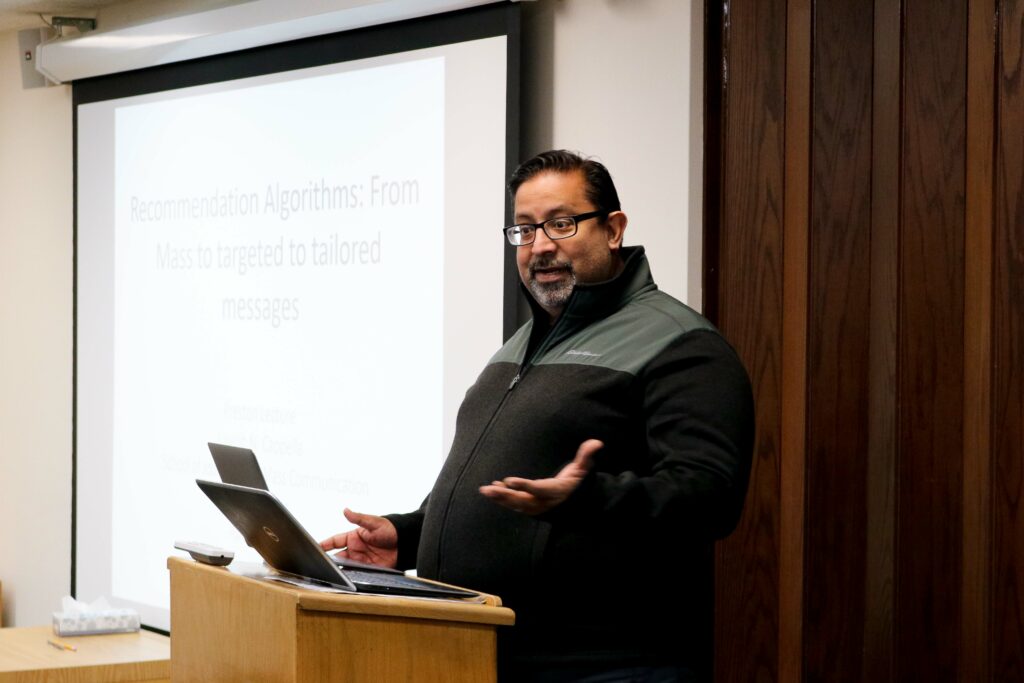 Dhavan Shah standing at a podium in front of a projector screen