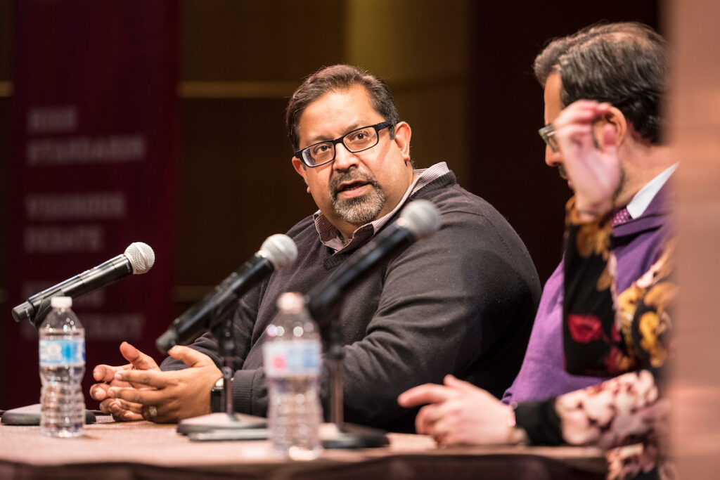 Dhavan Shah seated at a table speaking into a microphone