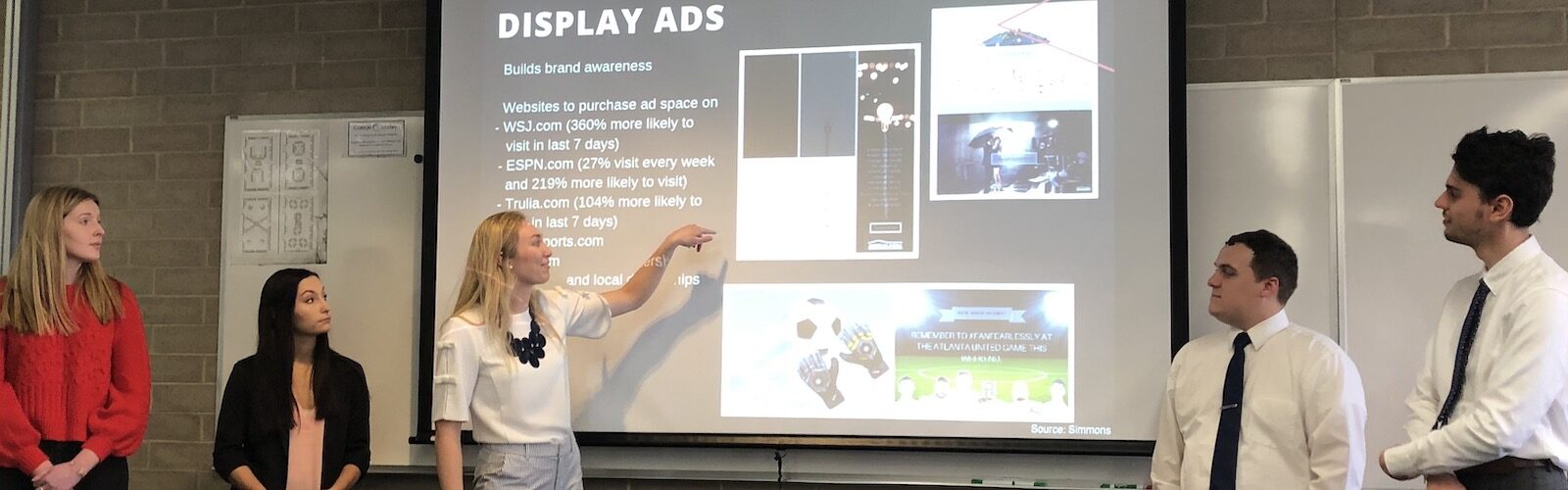 Students standing in front of a projector screen with a slide that reads "Display Ads"
