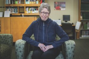 Professor emeritus Sharon Dunwoody smiles and sits in an arm chair in the Journalism Reading Room in Vilas Hall.