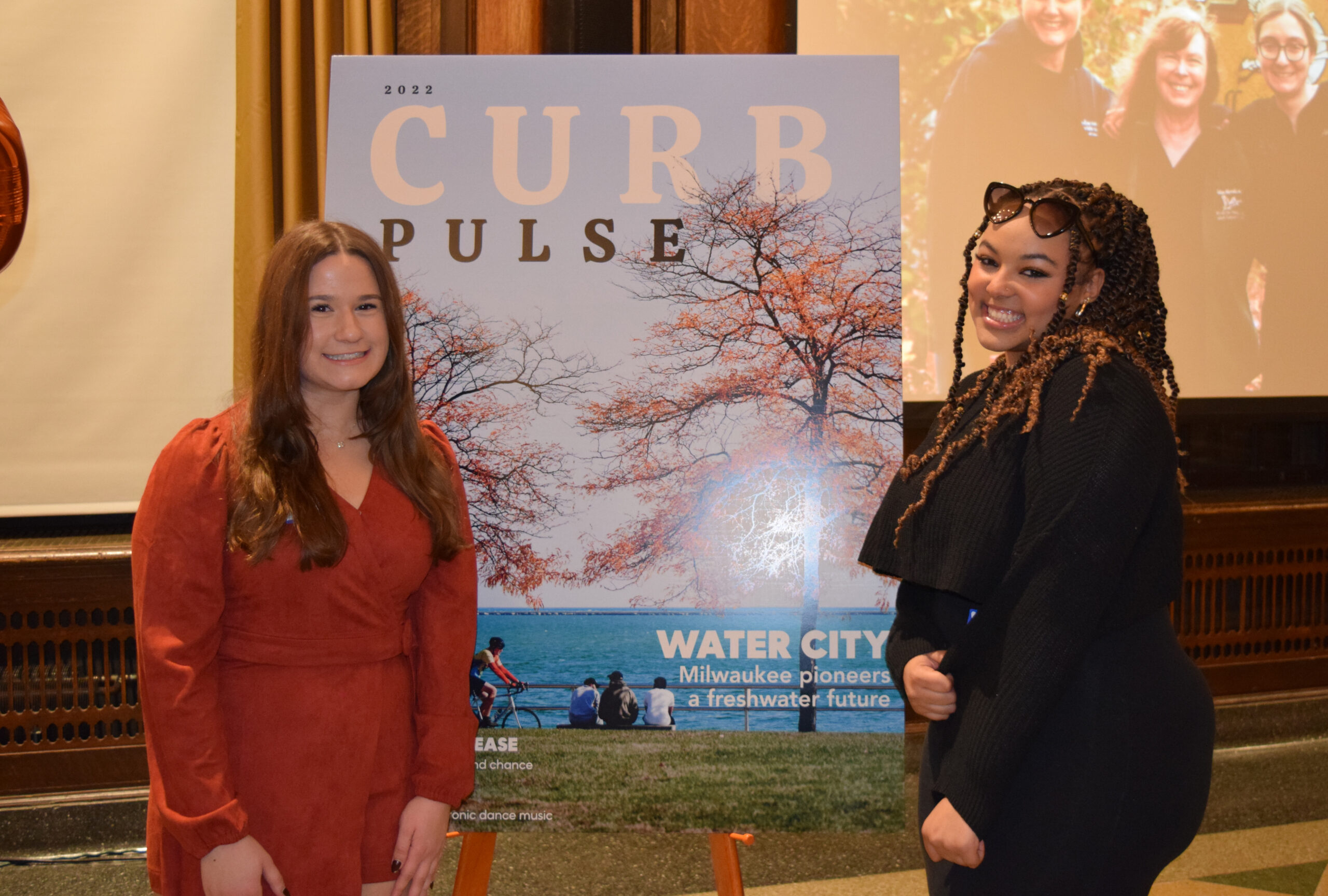 Two female students stand on either side of a foam board showing the cover of Curb magazine's "Pulse" issue at the Curb launch party on December 13, 2022 at the Memorial Union. 