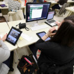 Journalism students working on a computer and table in a classroom